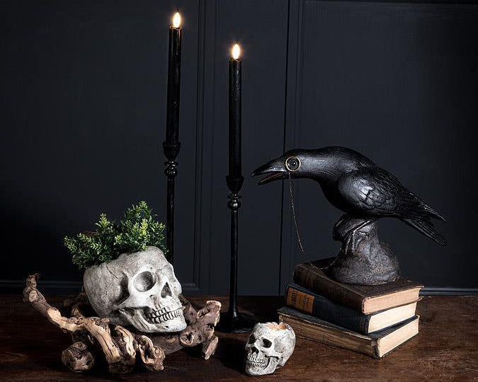 Decorative setup with skulls, candles, and a crow statue on a dark background
