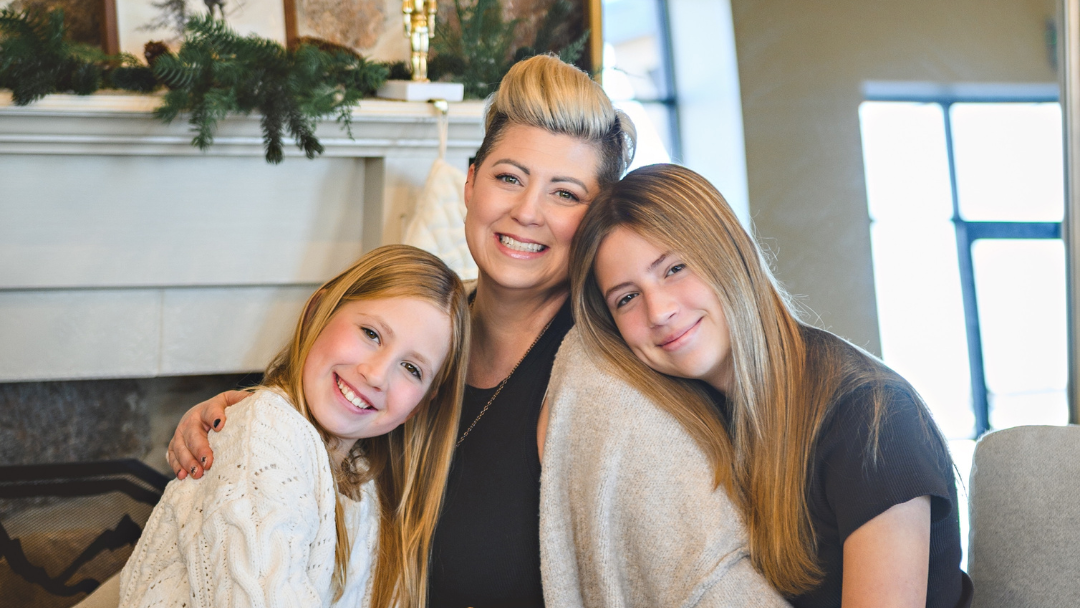 Woman and two young girls sitting together in a cozy living room with Christmas decorations.