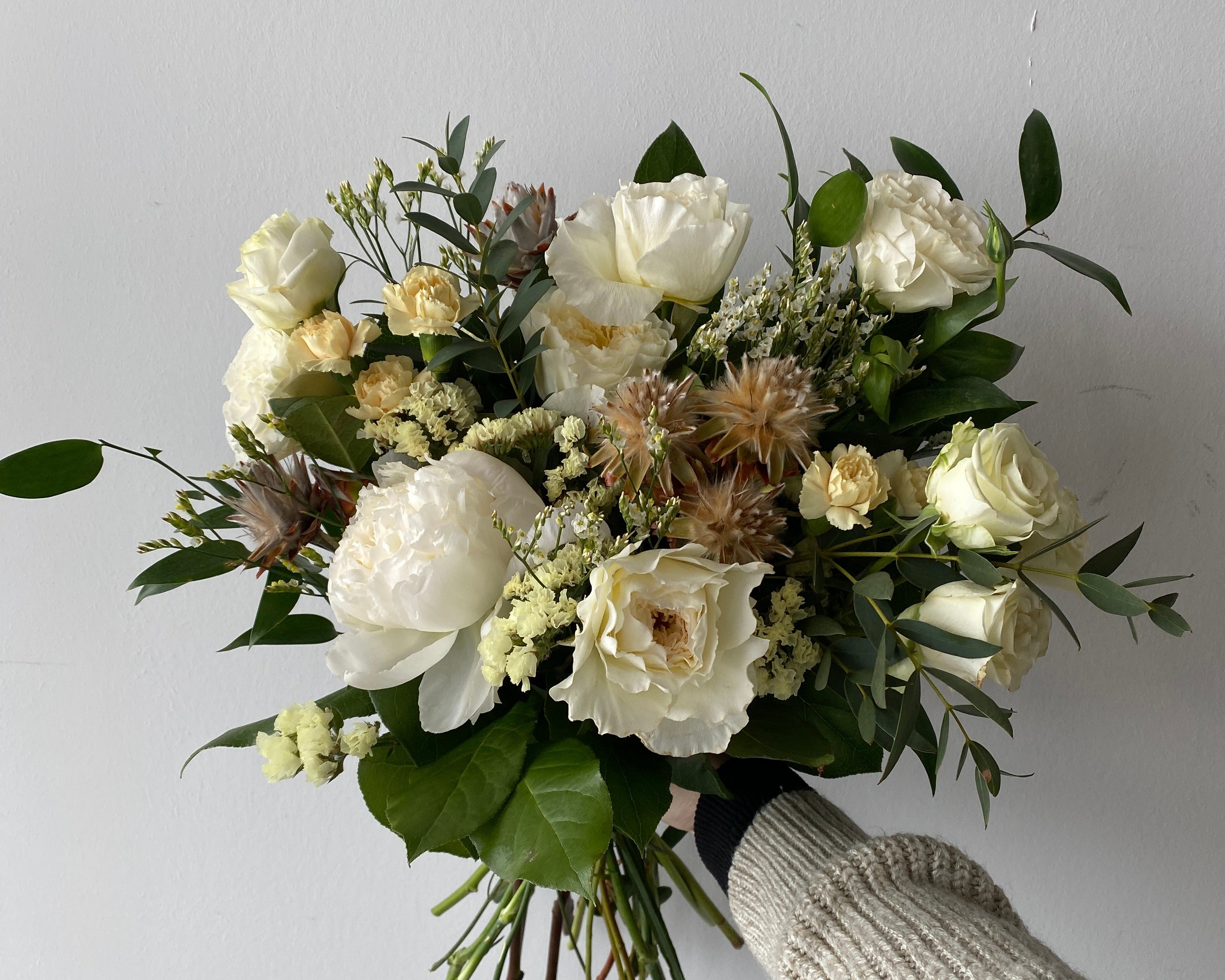 Bouquet of white and green flowers held by a person against a plain background