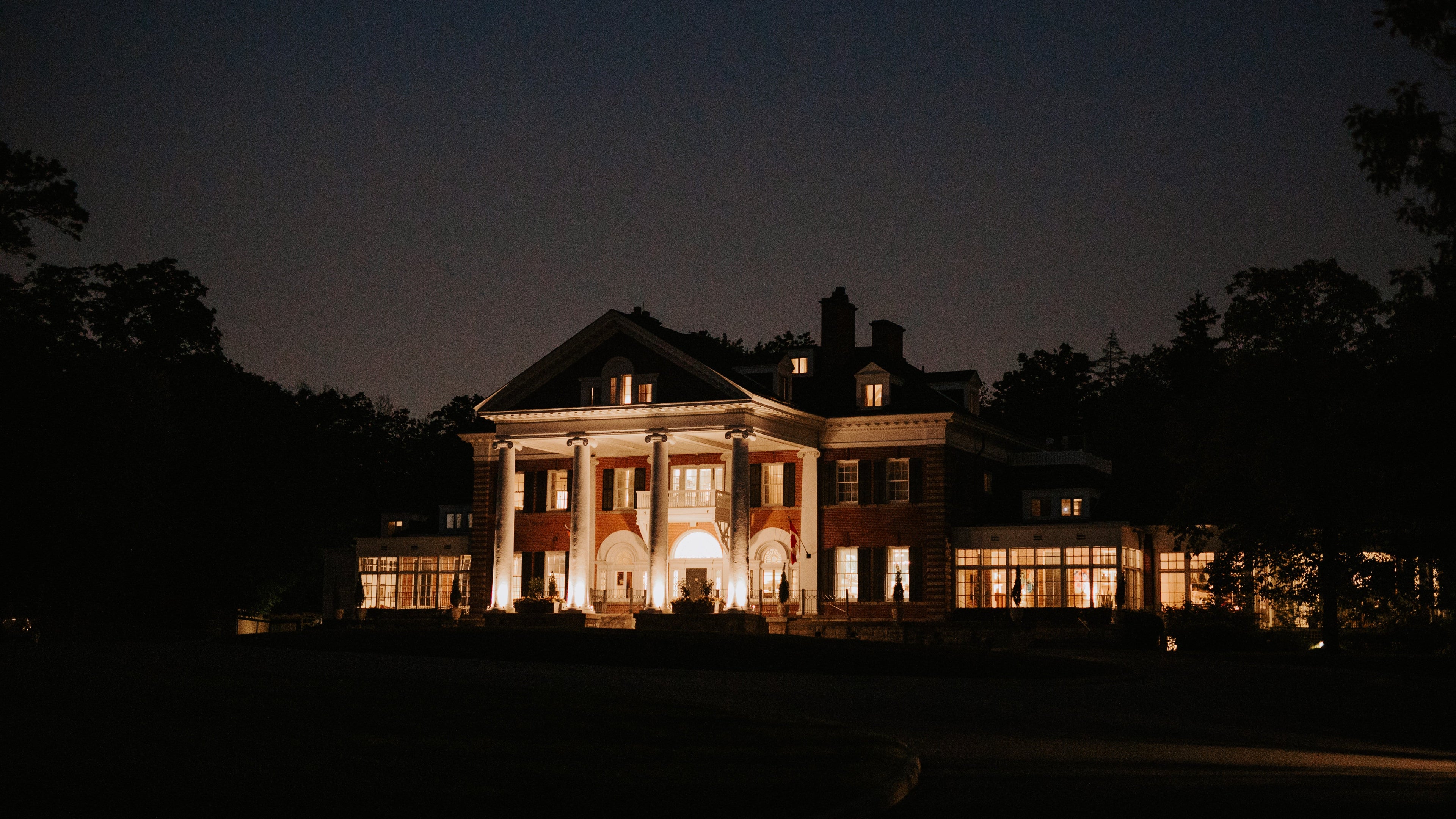 Elegant mansion illuminated at night with trees surrounding it.