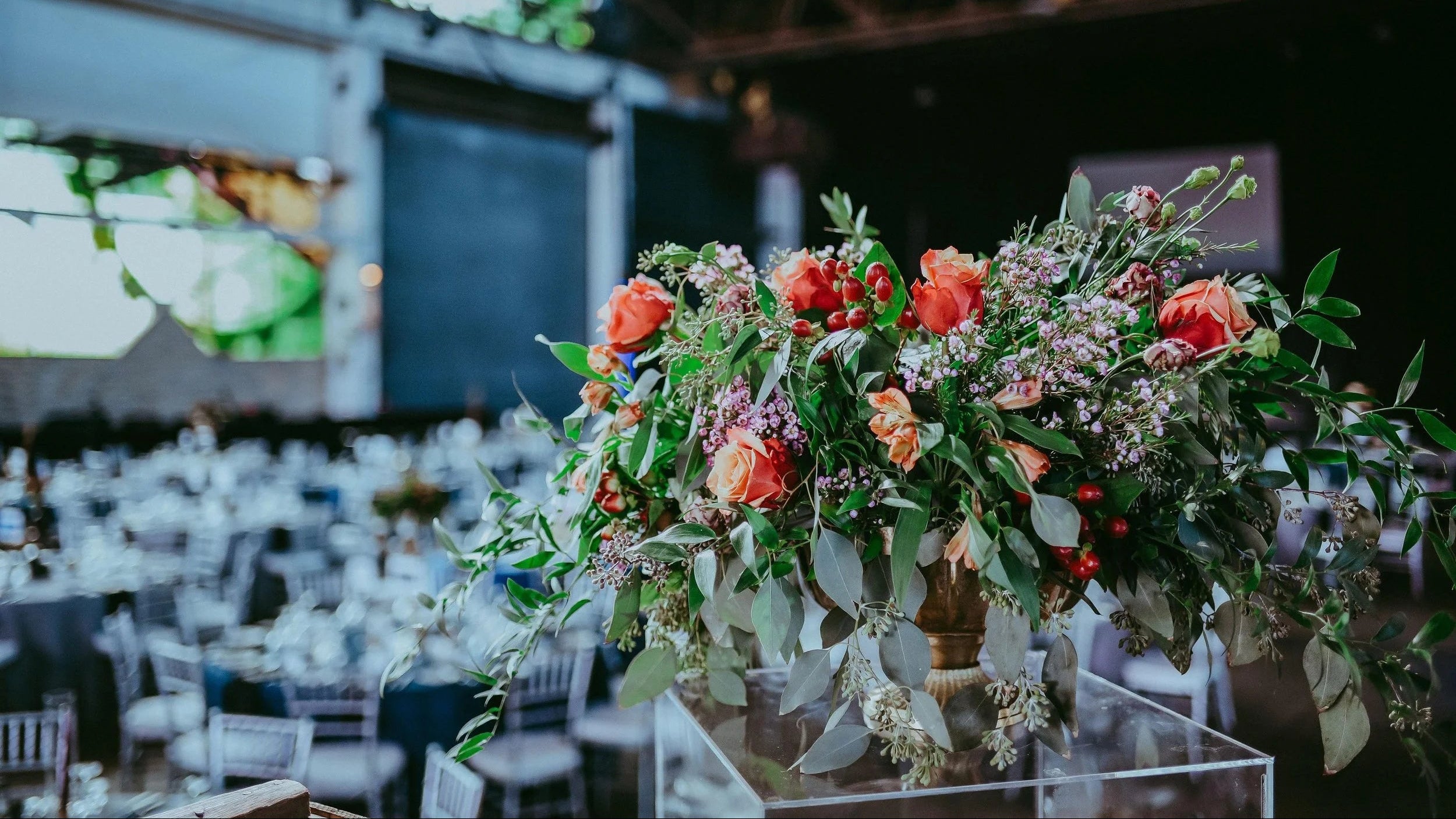 Decorative floral arrangement on a table in a large event space with tables and chairs.