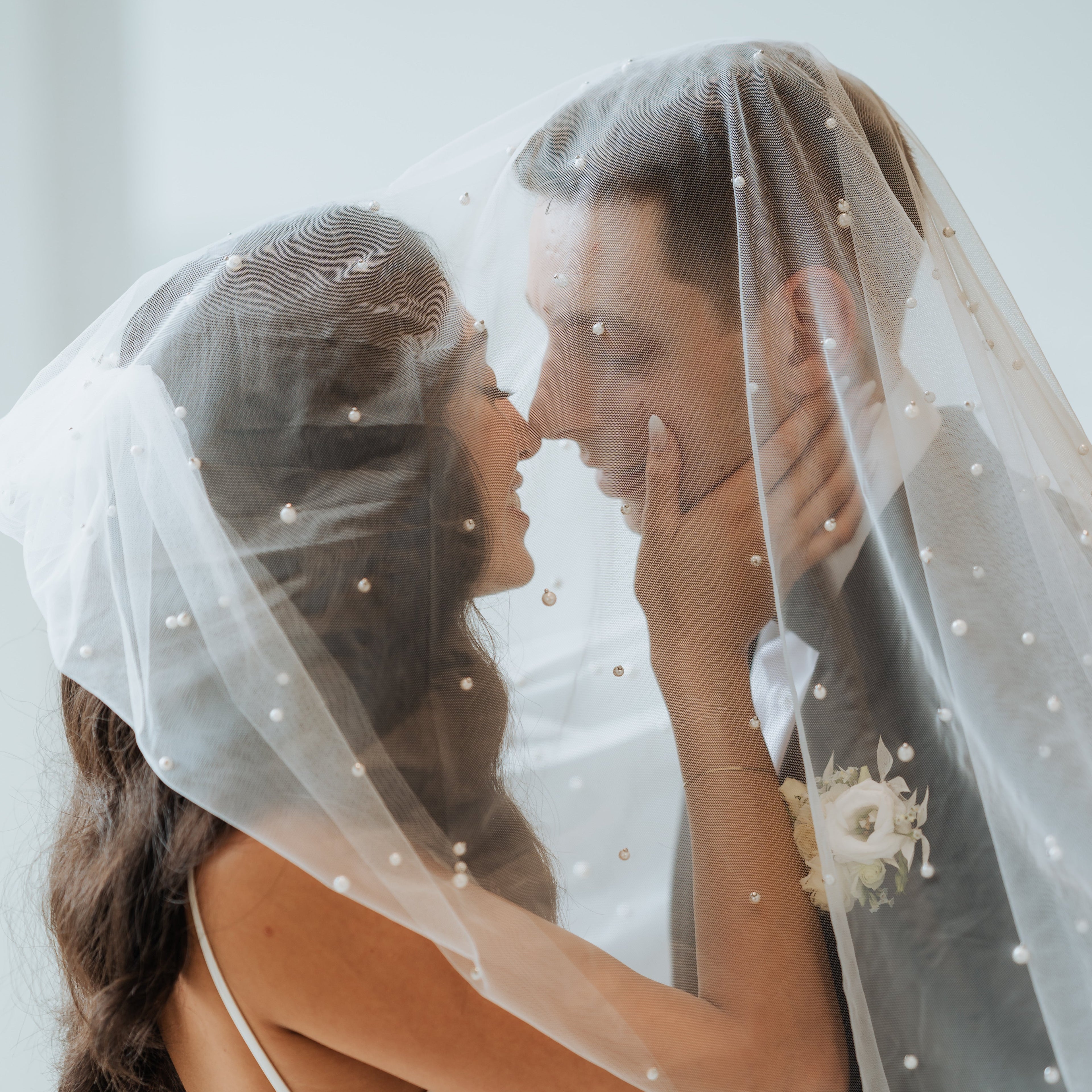 Couple sharing a kiss under a veil with floral details on a white background