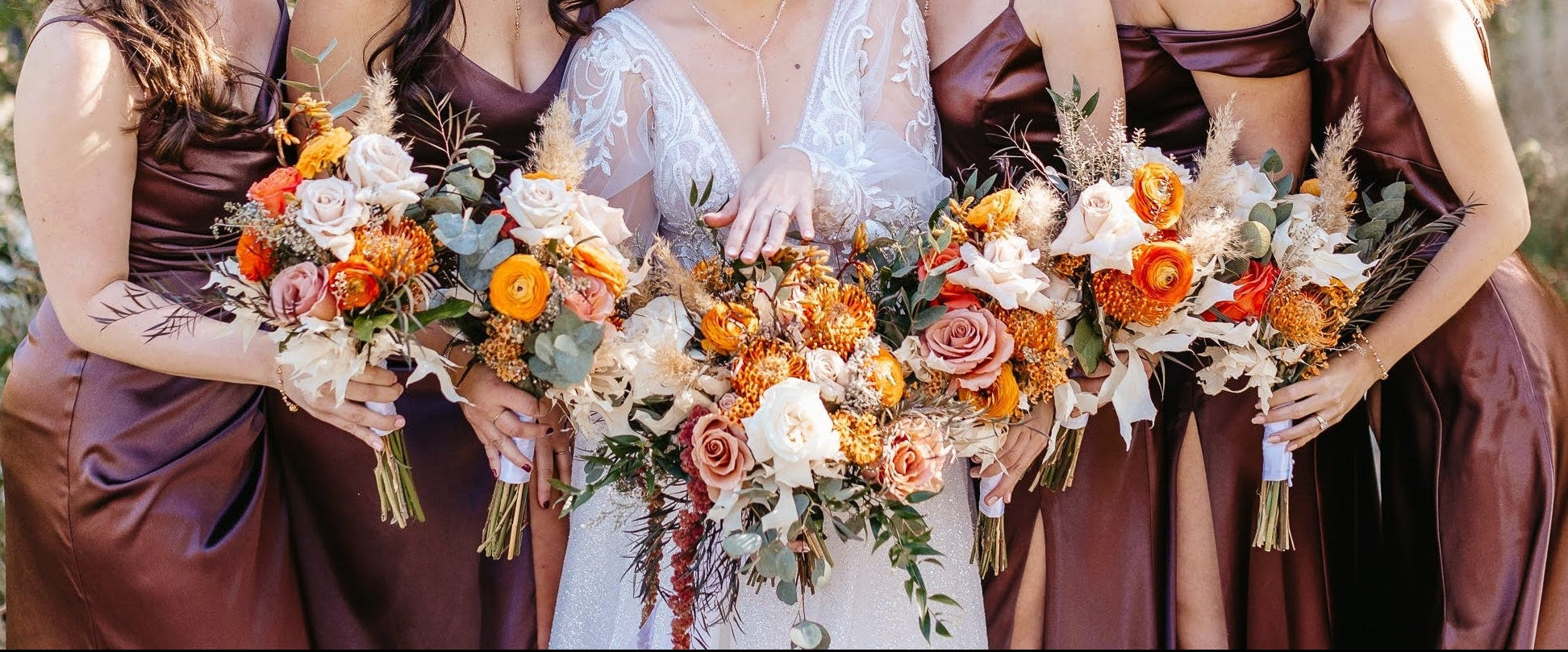Bride with bridesmaids holding floral bouquets outdoors