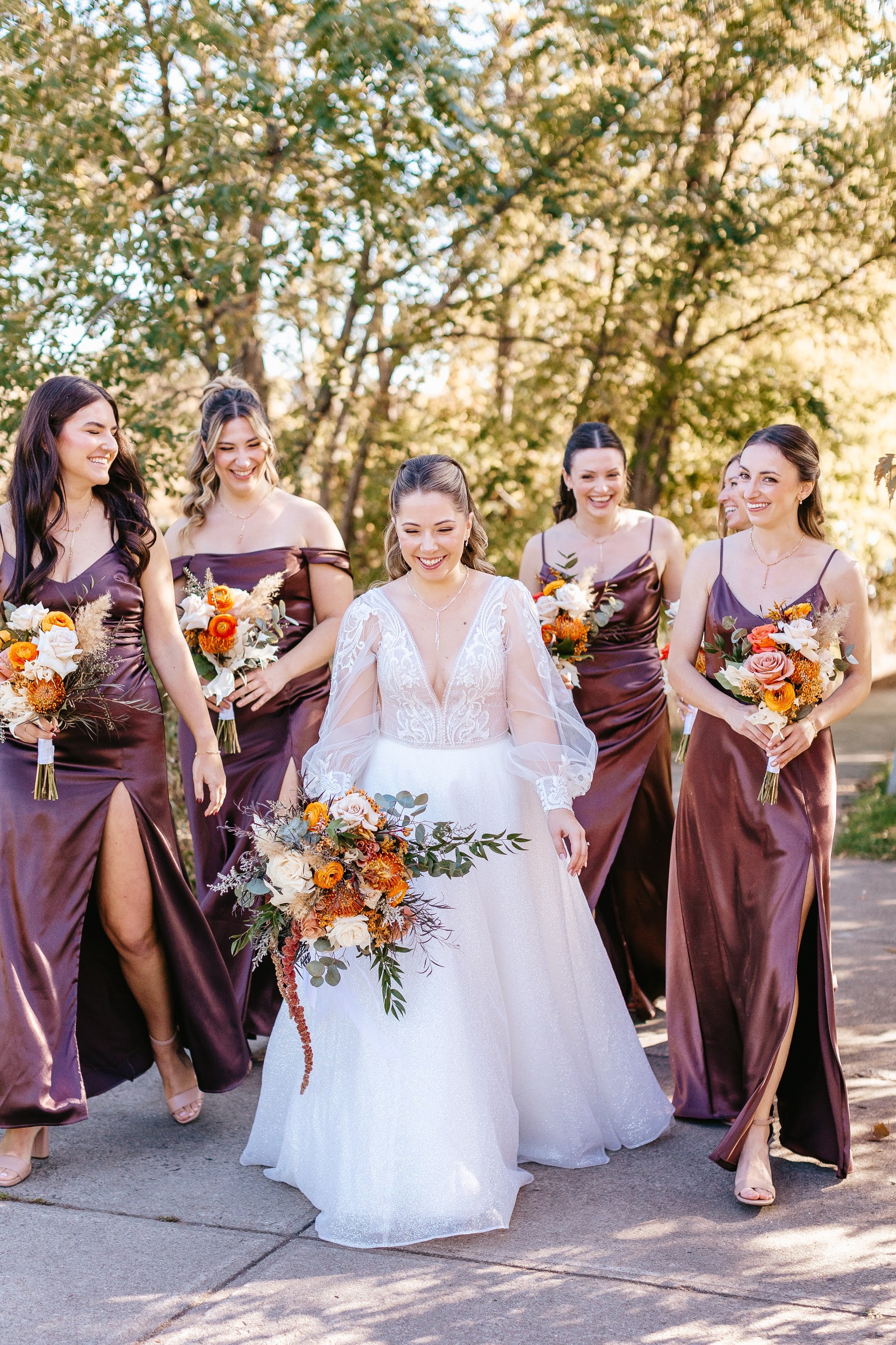 Bride in a white dress with bridesmaids in purple dresses holding bouquets outdoors.