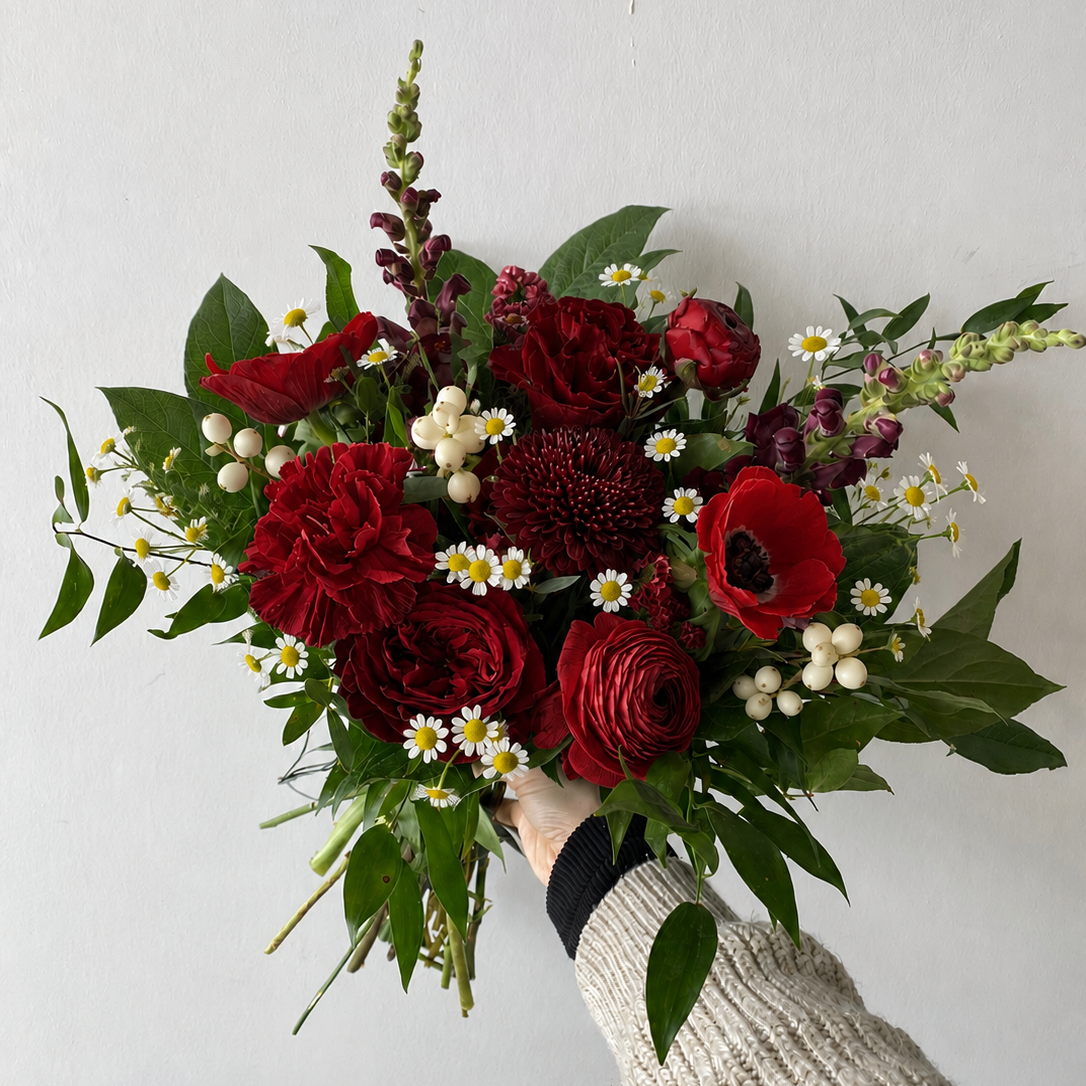 Bouquet of red flowers with green leaves held by a person wearing a beige sweater.