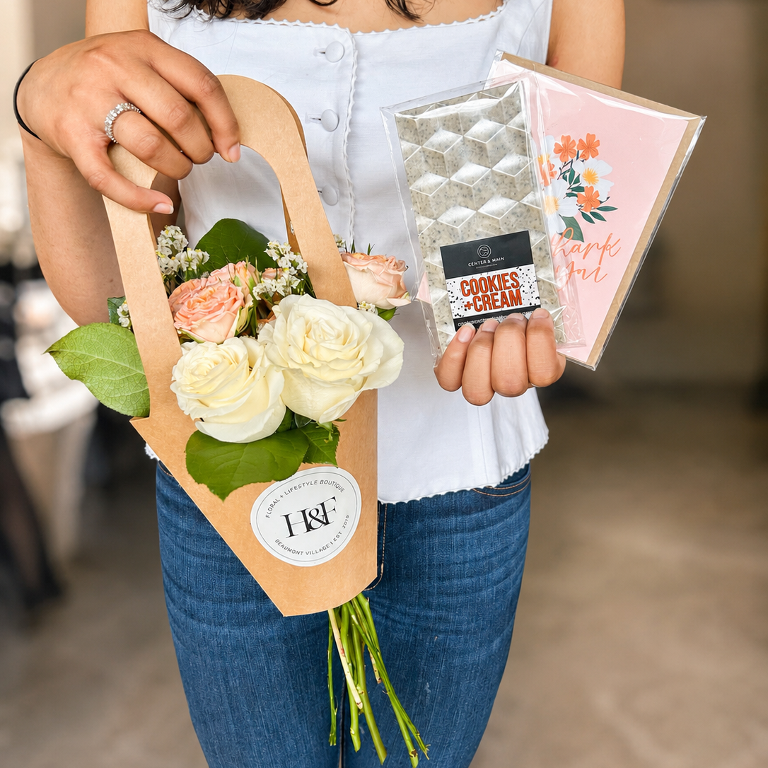 Person holding a bouquet of flowers and a chocolate bar and a greeting card