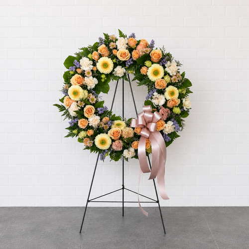 Floral wreath with a pink bow on a stand against a white background